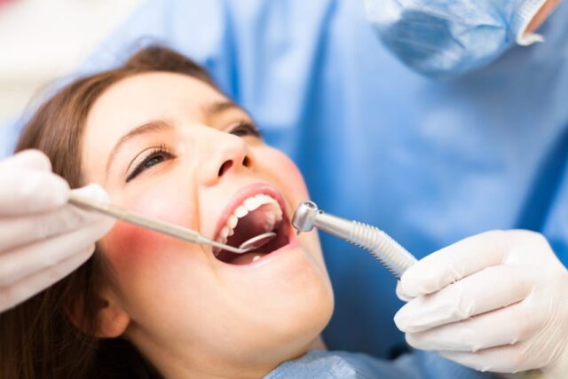 A dentist holding a mirror and drill near a female patient's mouth