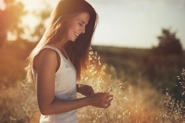 A young woman with dark hair walking in a field at sunset