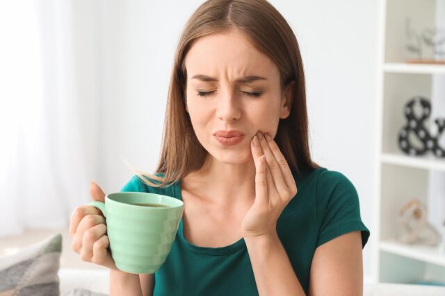 A woman grimaces as her sensitive teeth ache after drinking coffee, just before calling Summit Family and Cosmetic Dentistry for treatment.