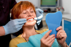 Woman looking at smile in mirror at dentist after dental implants exam