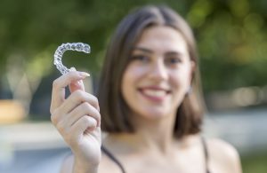 Smiling woman is holding a clear aligner